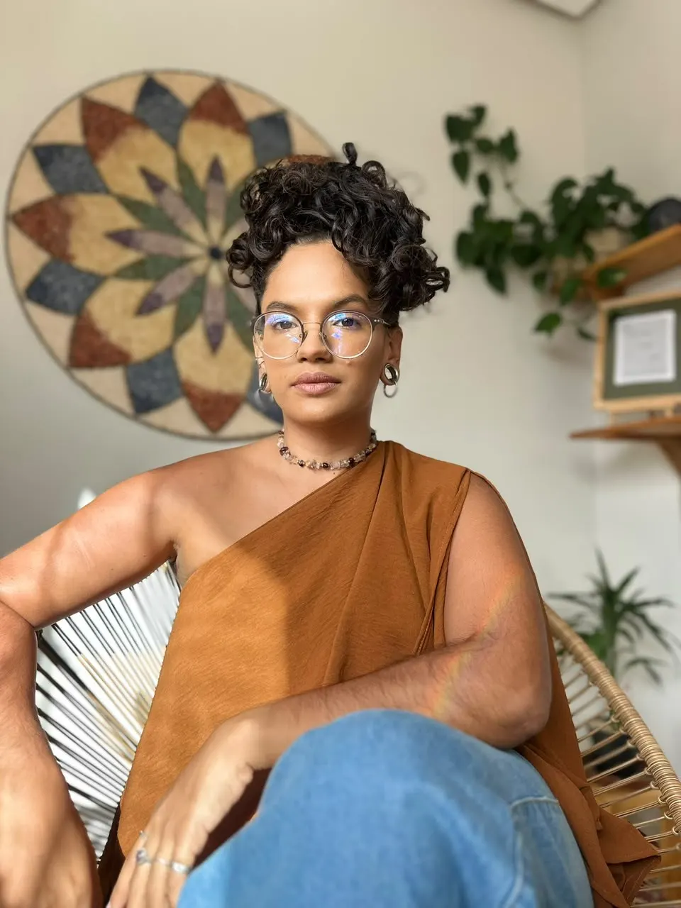 Vitória sentada numa poltrona de fibra, com uma mandala ao fundo